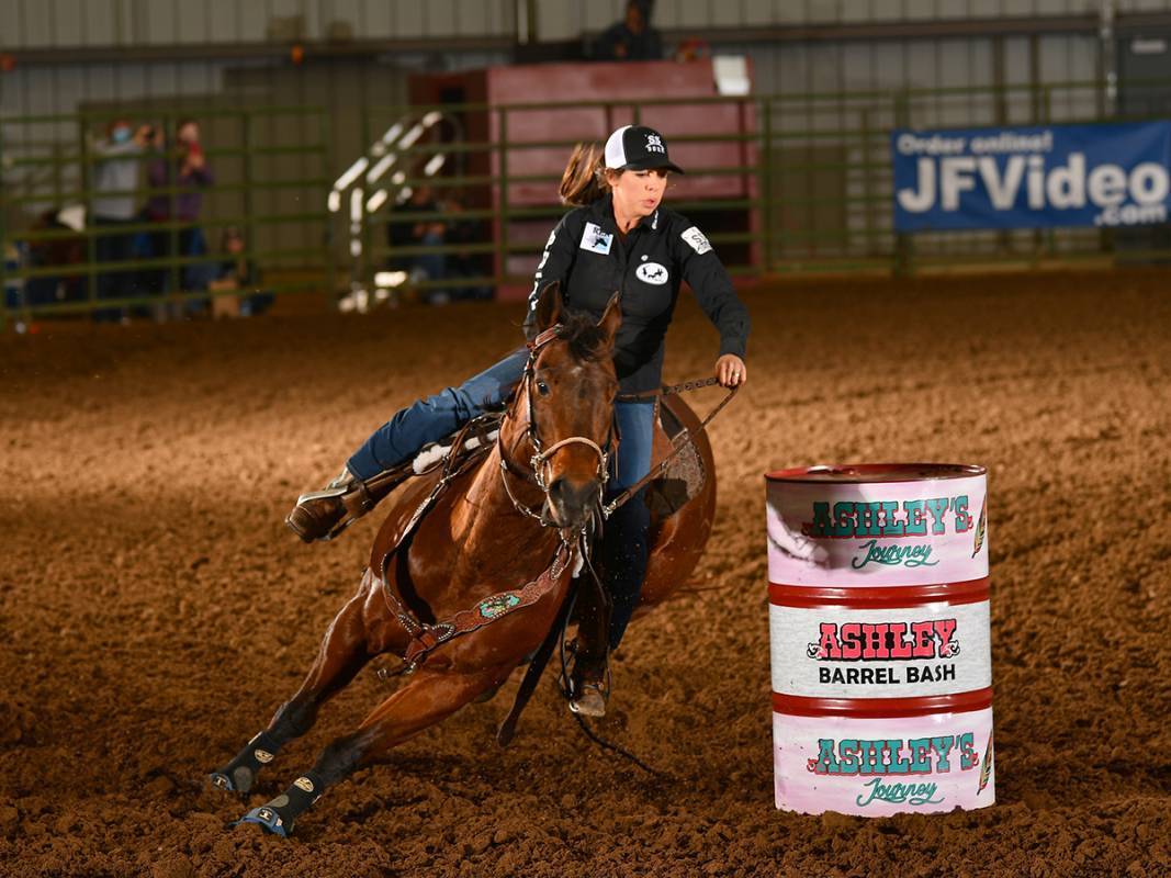 Barrel racer Alex Simpson Segyra completing a turn around a barrel on brown horse.