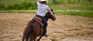 Cowgirl on horseback practicing barrel racing in corral